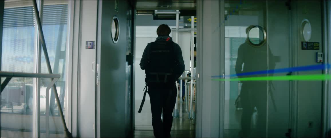 A man walks down a corridor while wearing a backpack