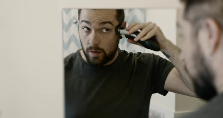 Man standing in front of mirror shaving his sideburns during COVID-19 lockdown