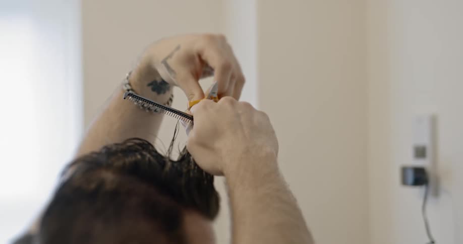 A man sits and cuts his own hair during COVID-19 lockdown