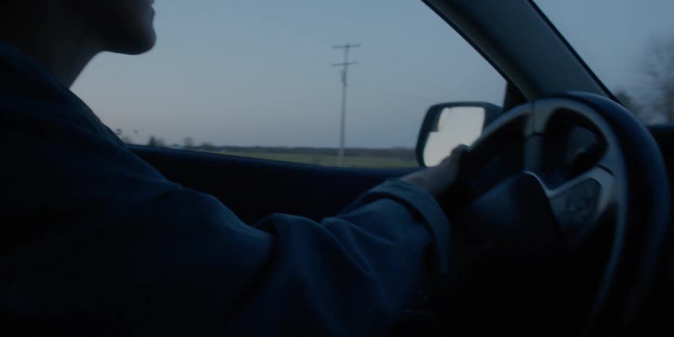 A woman turns a car around and drives down a rural road at sunset