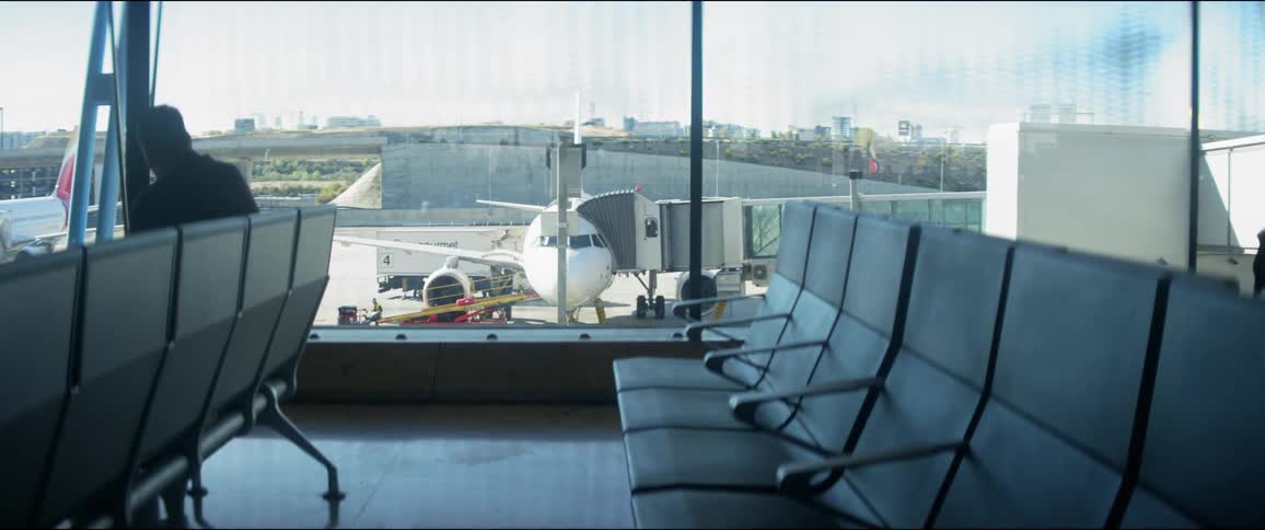 Man sits near window reflecting other people and showing view of airplanes