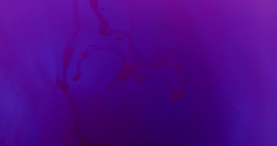 Red dye drips down and sinks slowly into blue glowing liquid