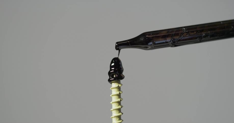 A dropper drips black oil onto the point and threads of a screw
