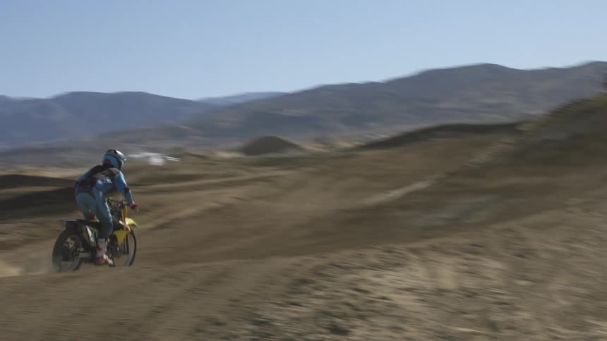 A motorcyclist jumps a bike over a hill on a dirt track