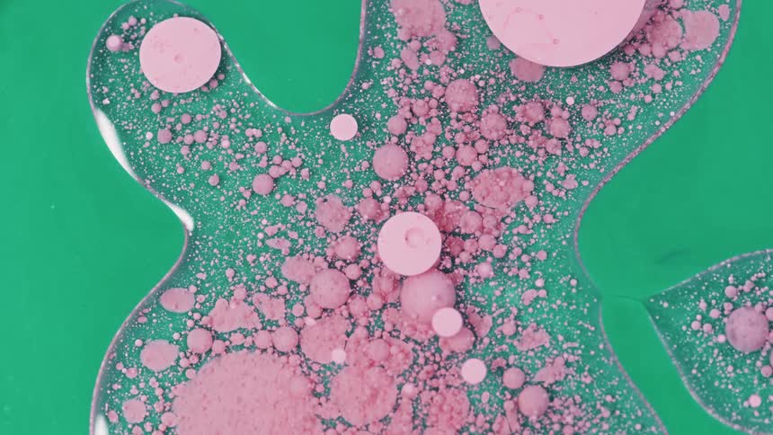 Pink globs float in clear liquid against green background