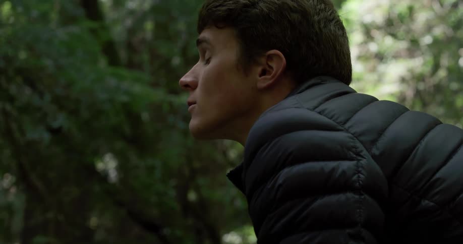 Side view of a man standing and looking up in the dense forest