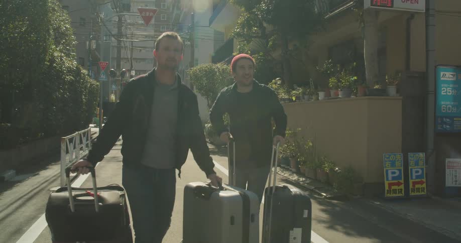 Two men pull their luggage down a street