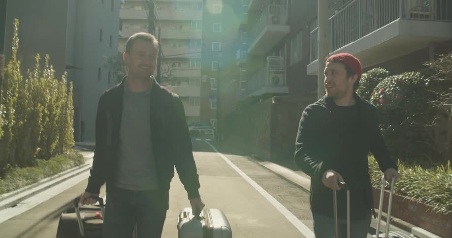 Two men walk down the street with suitcases