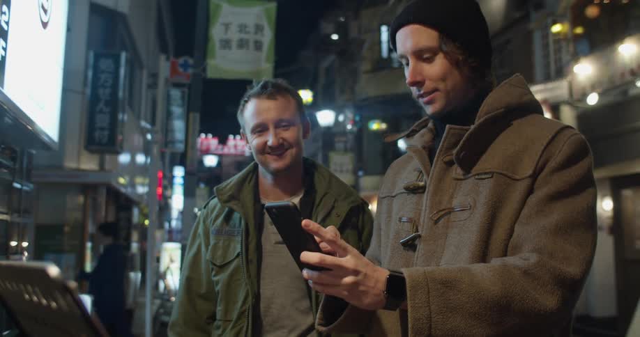 Two men stand outside of a restaurant in a big city