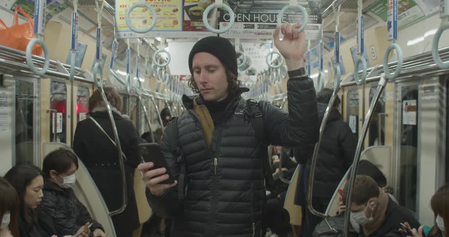 A man stands in the middle of a packed train car and uses his smart phone