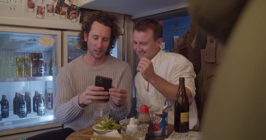 Two men sit at a table in a restaurant and look at a cell phone