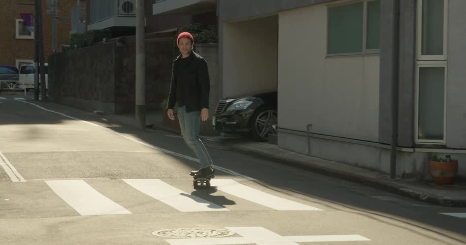 A man skateboards down a neighborhood street as a pedestrian walks by and a person bikes past