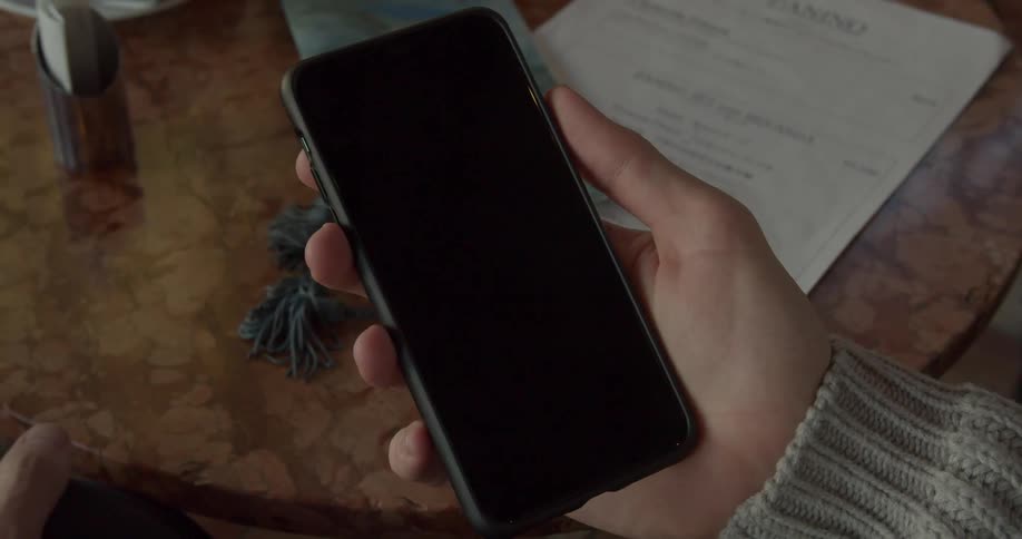A woman is holding a cell phone in her hand that is turned off