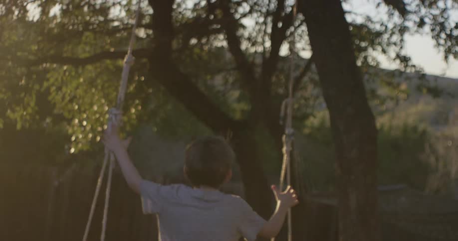 A boy running through a yard and climbing on a swing