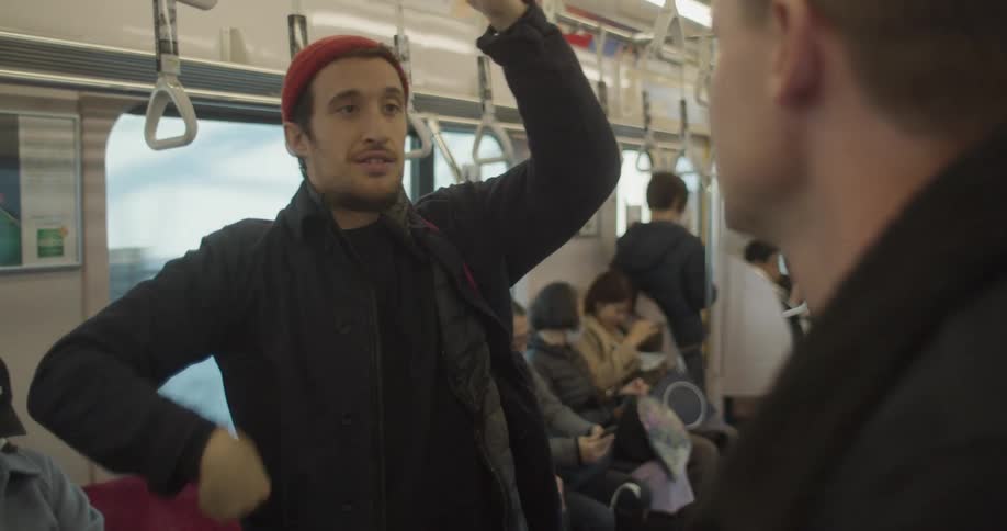 Two men stand and talk on a crowded subway