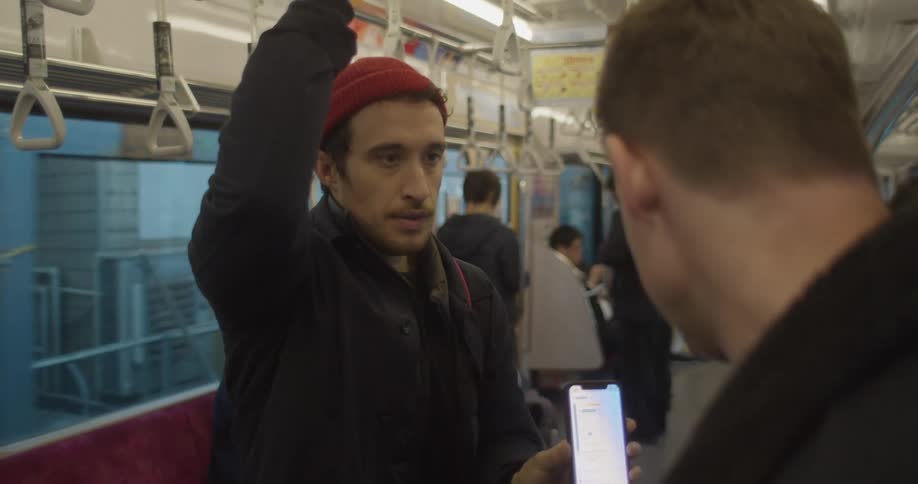 A man on a train shows someone else something on his phone