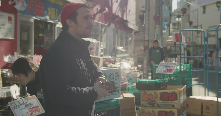 A man standing in front of a shop with a smart phone then starts to walk away