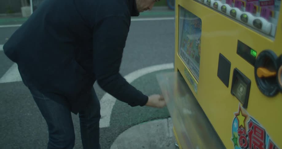 Man obtains drink from machine as bicyclist passes
