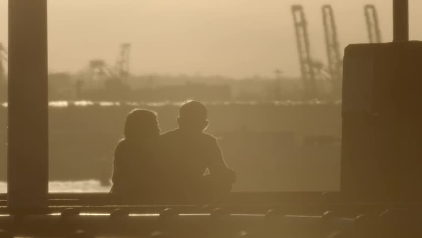 A man and woman sit together with construction cranes in front of them
