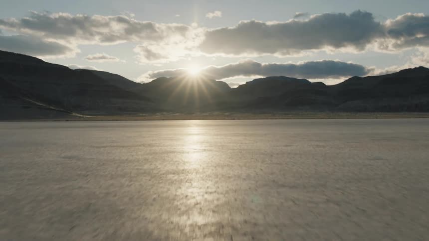 A cracked desert surface sits in front of a mountain range at sunset