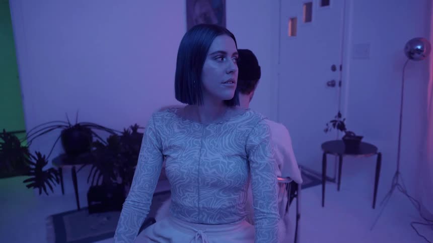 Man and woman sit in chairs back to back in a blue lit room