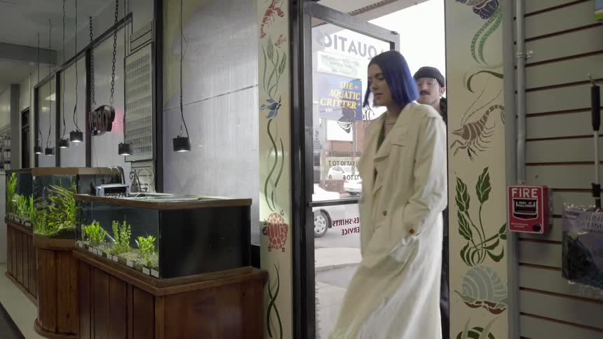 Male opens door for female while laughing and talking and they enter a store with several aquariums along the front wall