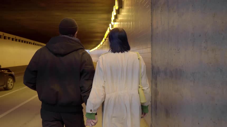 A couple walk through a traffic tunnel while holding hands