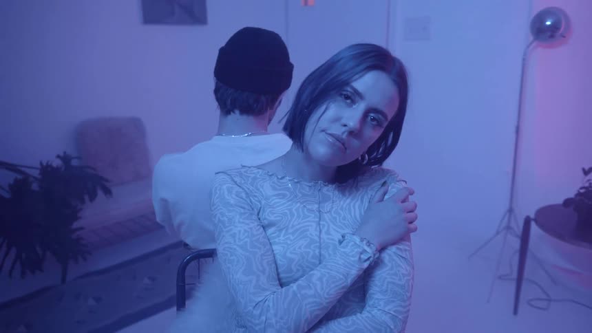 A woman and man sit back to back in chairs in a color lit room