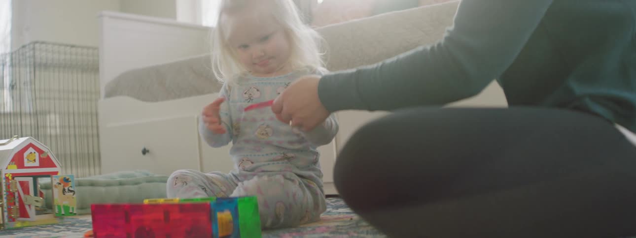 A mother and daughter sit on the floor in a room and play with building blocks