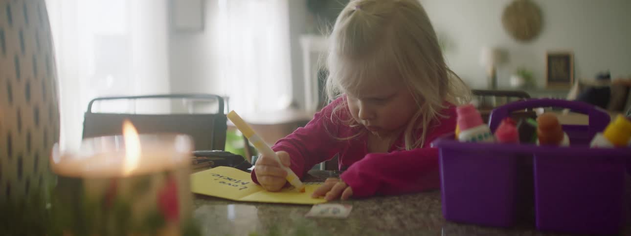 A child writing a card as a candle burns