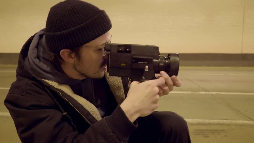 A man with a camcorder shooting and talking while on one knee
