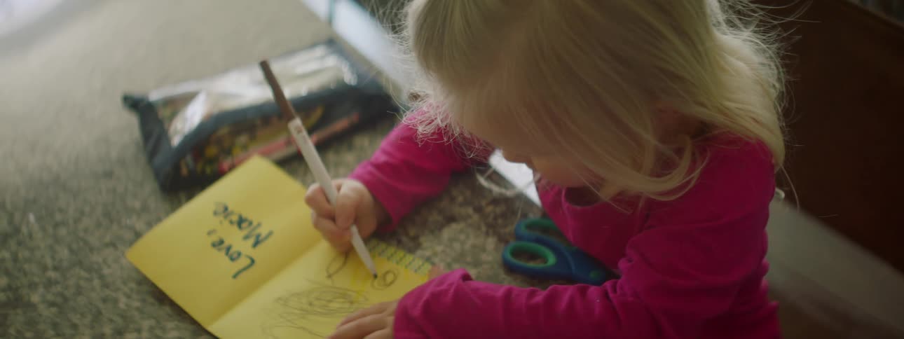 A little blonde girl uses a marker to draw inside a home made card