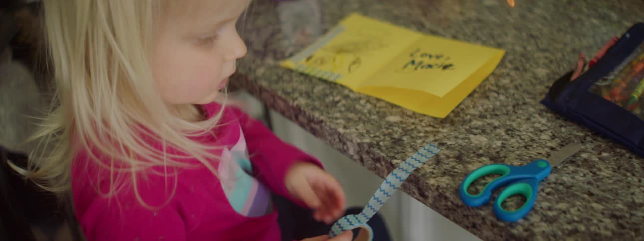 A young girl cuts a piece of decorative tape for an art project while sitting at a kitchen counter