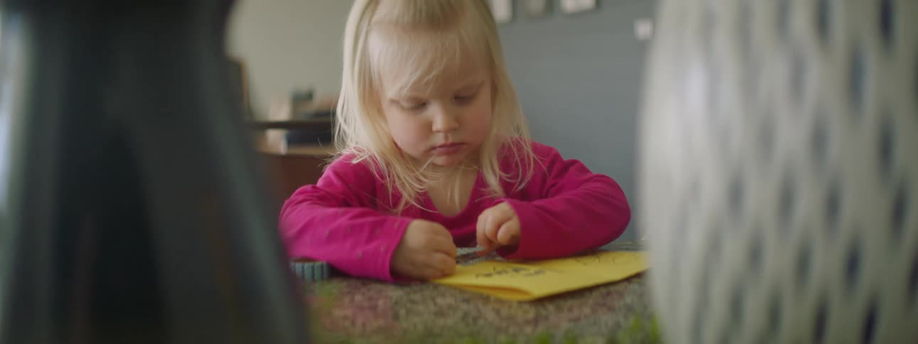 Little blonde girl placing tape on a yellow card she created