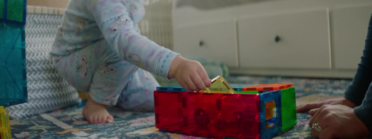 A little girl builds with toys as her mother watches