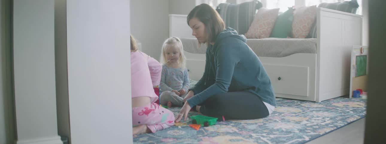 A woman and two children play with toys together on the floor