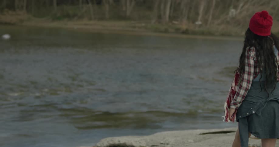 A woman walks towards a river in the woods