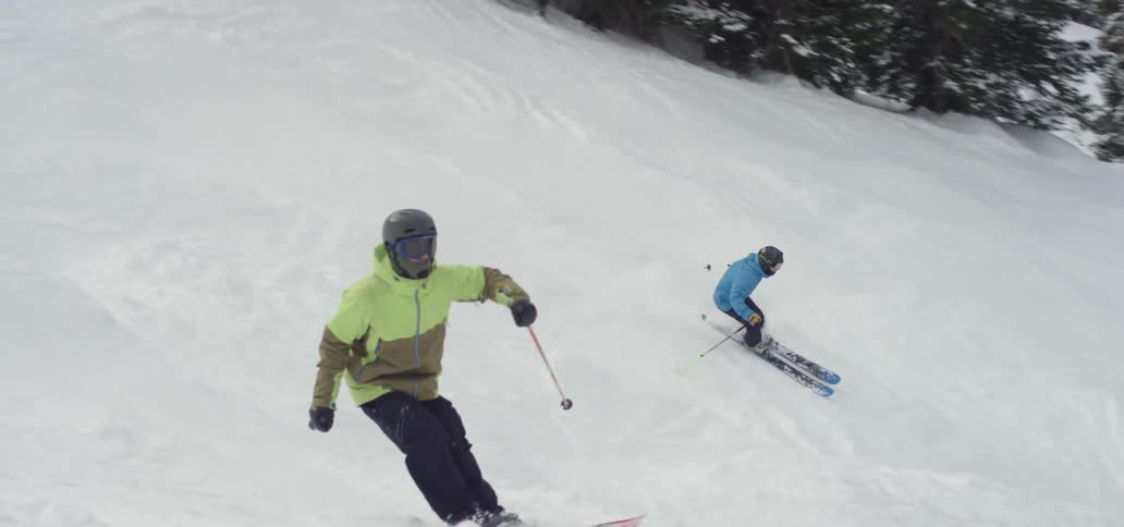 Two skiers ski down a mountain slope side by side