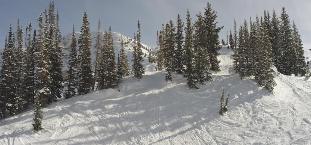 A skier doing a back flip of a mountain ridge before landing and continuing down the slope