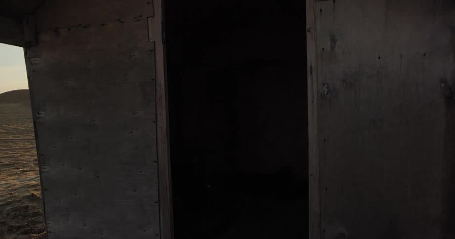 A wooden shack with a dark doorway sits in the desert