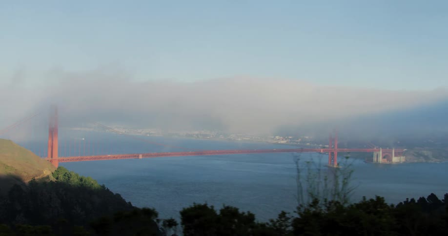 Parts of san francisco are visible through fog behind the golden gate bridge