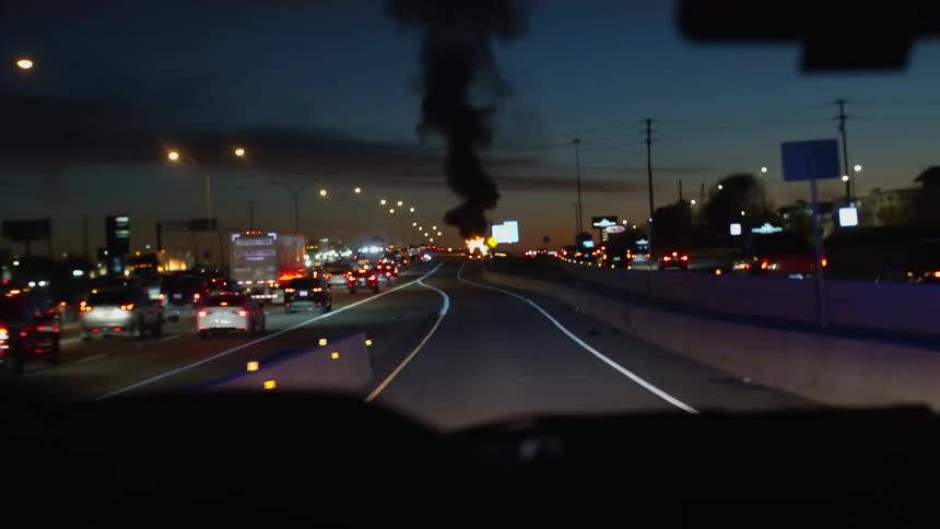A fire truck drives towards a fire and black smoke as other cars drive on the road