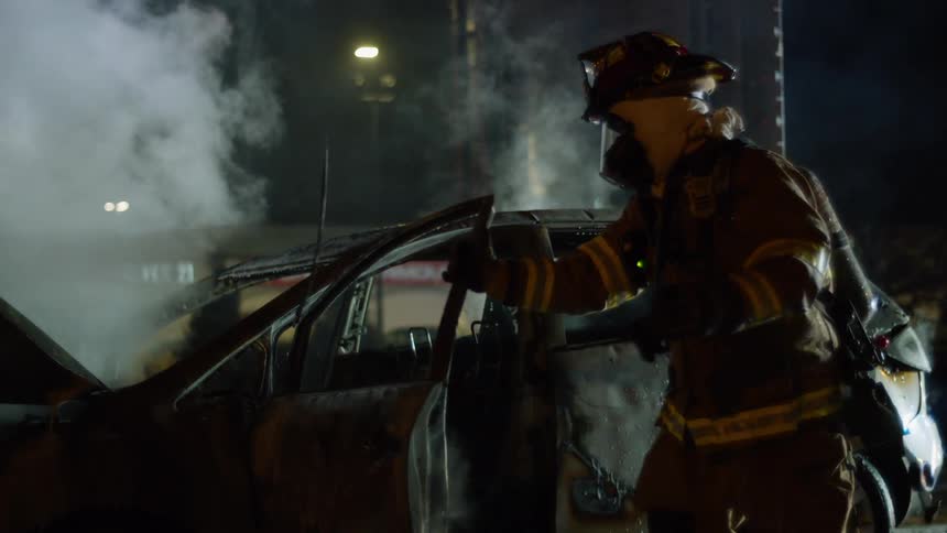 A firefighter pulls open the door on a burnt out car