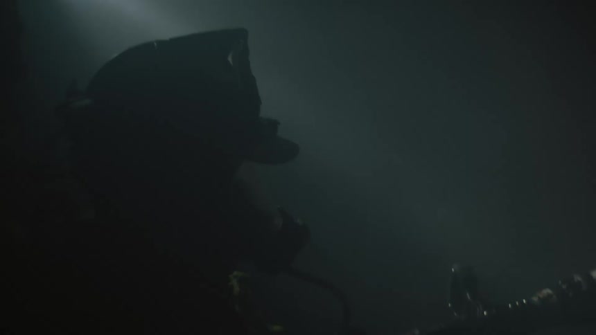 A firefighter standing in smoke sprays water