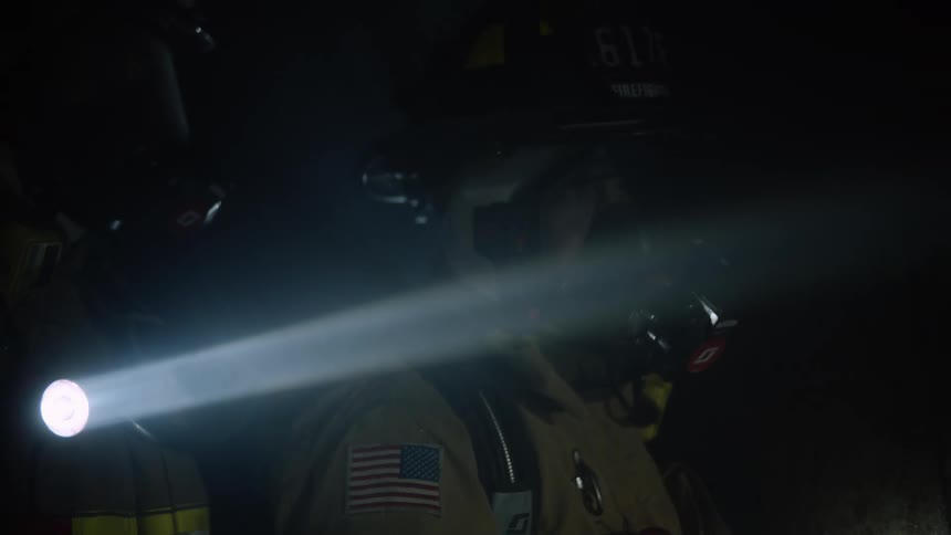 Firefighters use flashlights to navigate a dark smoky room