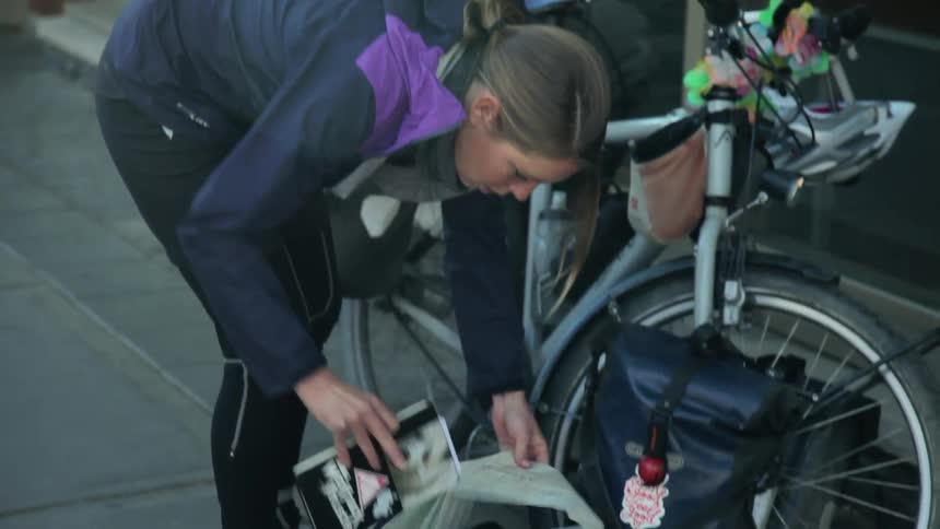 A white female bicyclist takes a book out of a folded map