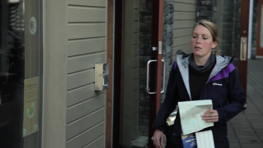 A woman carrying maps walks out of a building