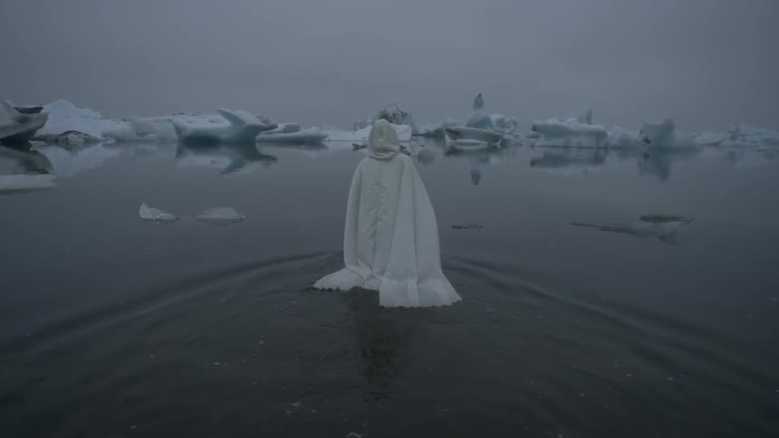 A person wearing white robes is walking into the water towards floating ice