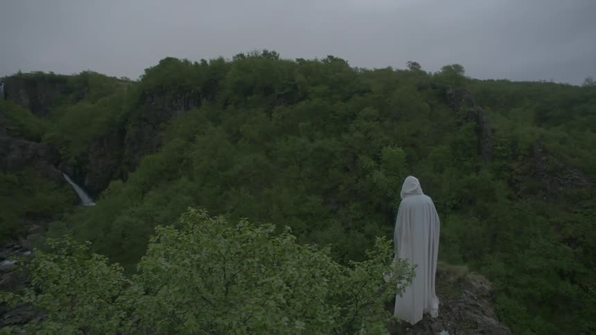 A white-cloaked figure standing on a boulder