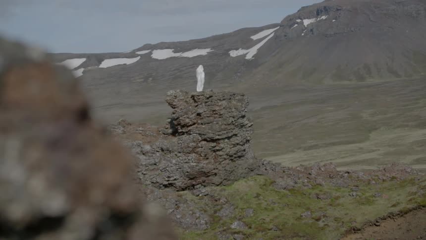A white cloaked figure stands on top of a rock formation